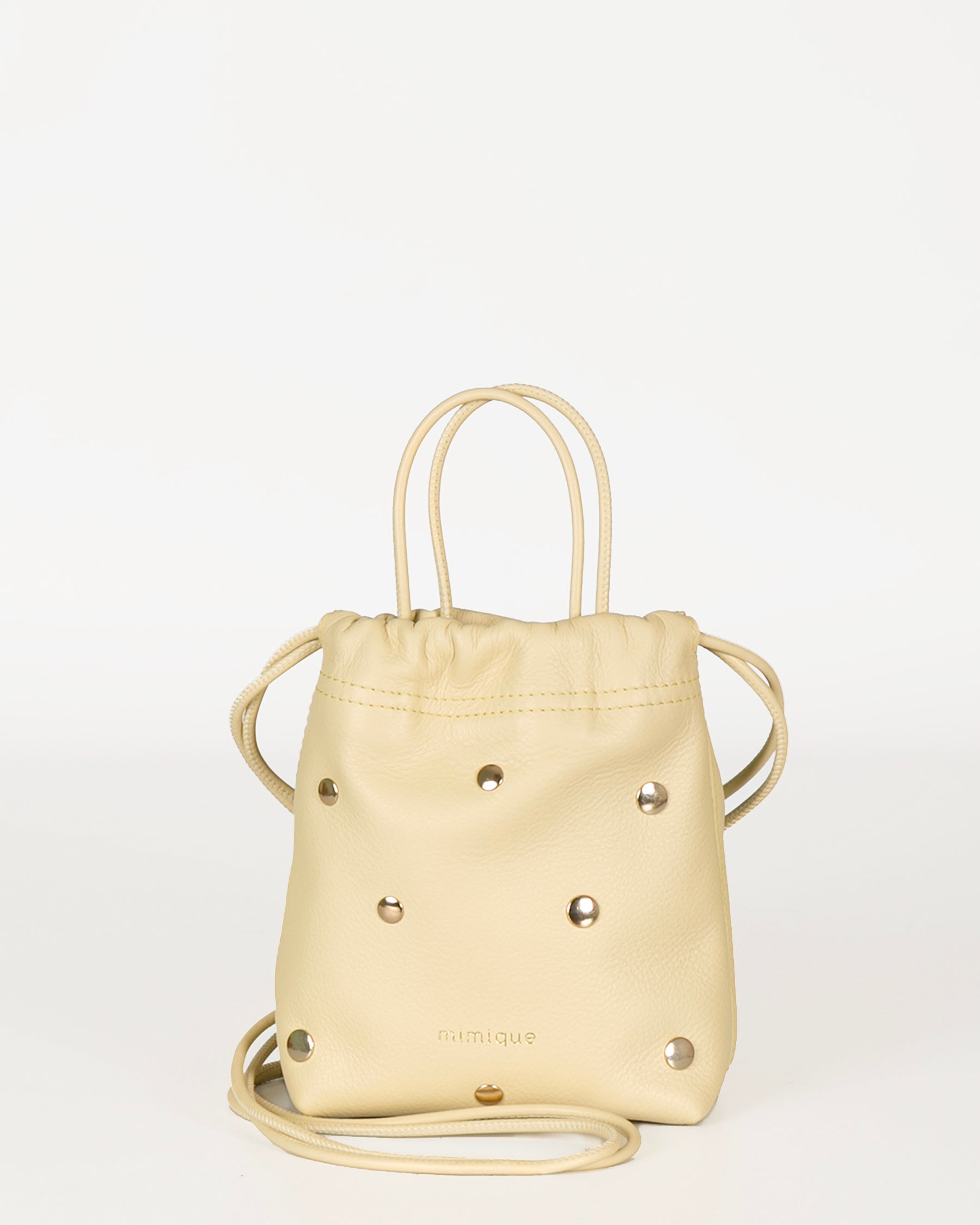 Mini bolso bombonera de piel para mujer Cue dots color mantequilla con tachuelas metálicas. Bandolera cómoda, ligera y atemporal. Piel de máxima calidad. Made in Spain