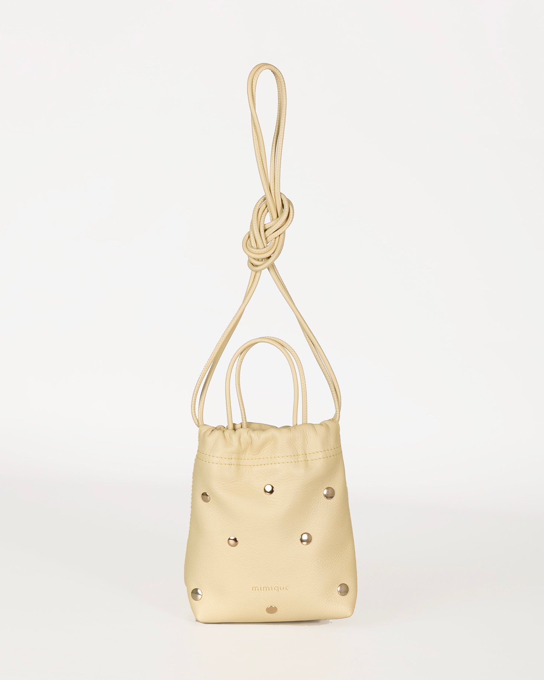 Bolso pequeño de piel para mujer Cue dots color vainilla con tachuelas metálicas con acabado de oro viejo. Diseño de bombonera para llevar como bandolera cómoda, ligera y atemporal. Piel de máxima calidad. Hecho a mano en España