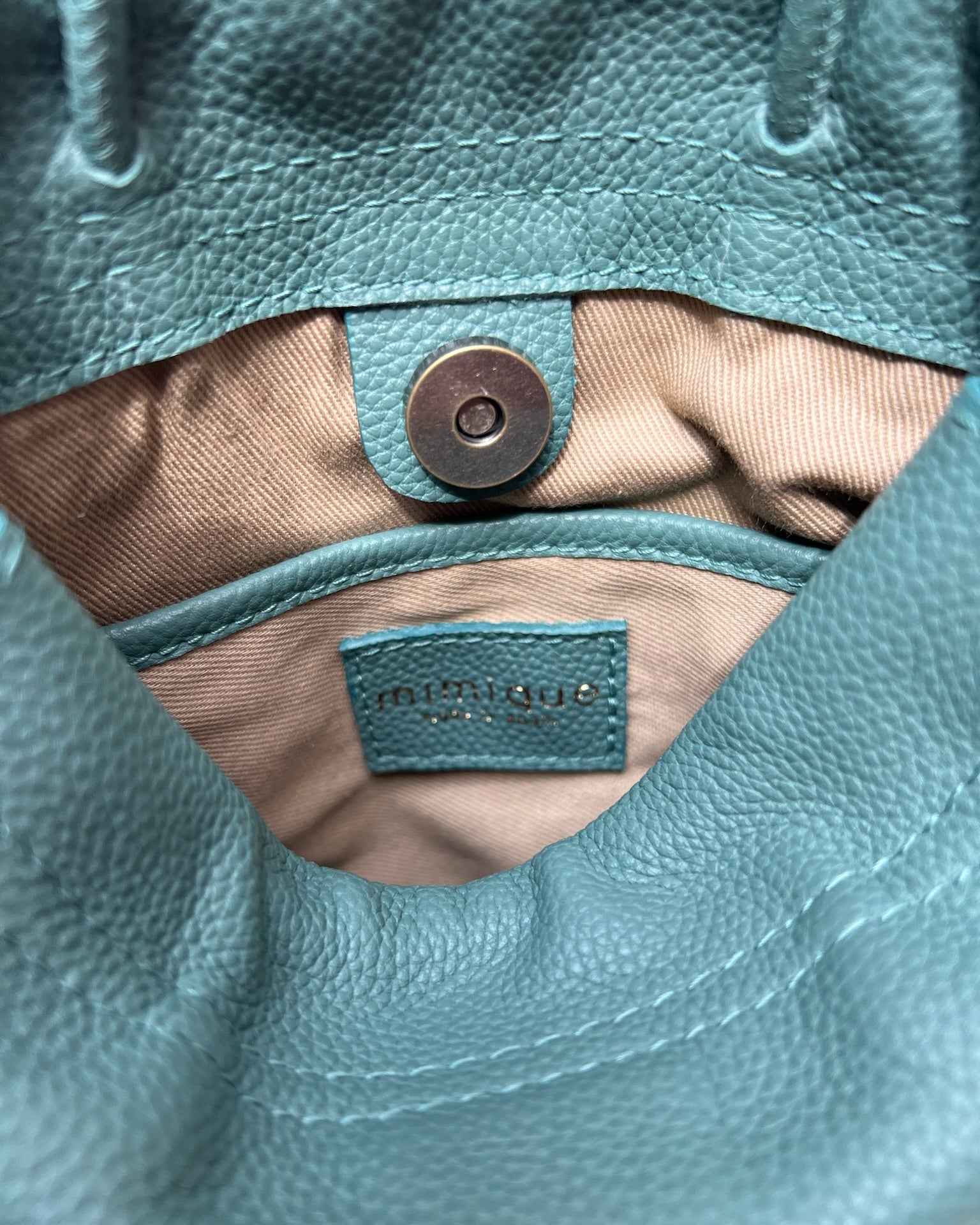 Bolso bombonera Mimique Cue en azul aguamarina, piel de gran calidad, bandolera cómoda y ligera hecha a mano en España. Bolsillo y forro interior